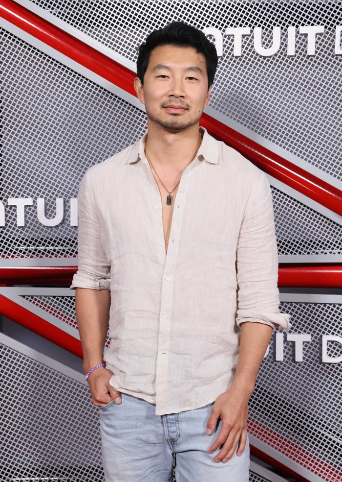 Person in a casual shirt and jeans posing at an event with a textured background and red accents