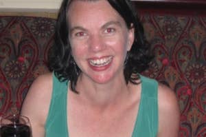 Person smiling while holding a wine glass in a patterned setting