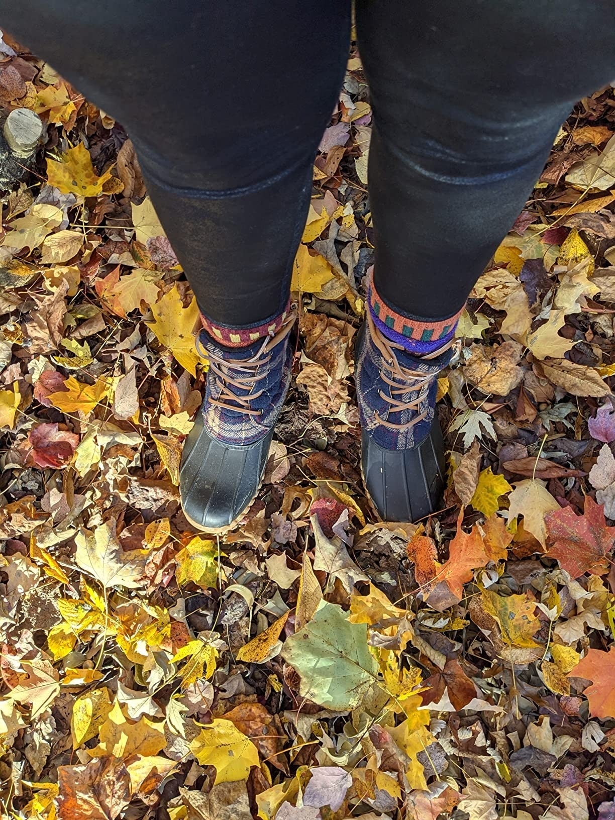 a reviewer wearing the plaid boots and leggings lasting  connected  colorful autumn leaves scattered connected  the ground