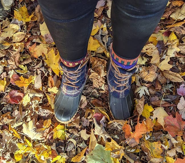 a reviewer wearing the plaid boots and leggings lasting connected colorful autumn leaves scattered connected the ground