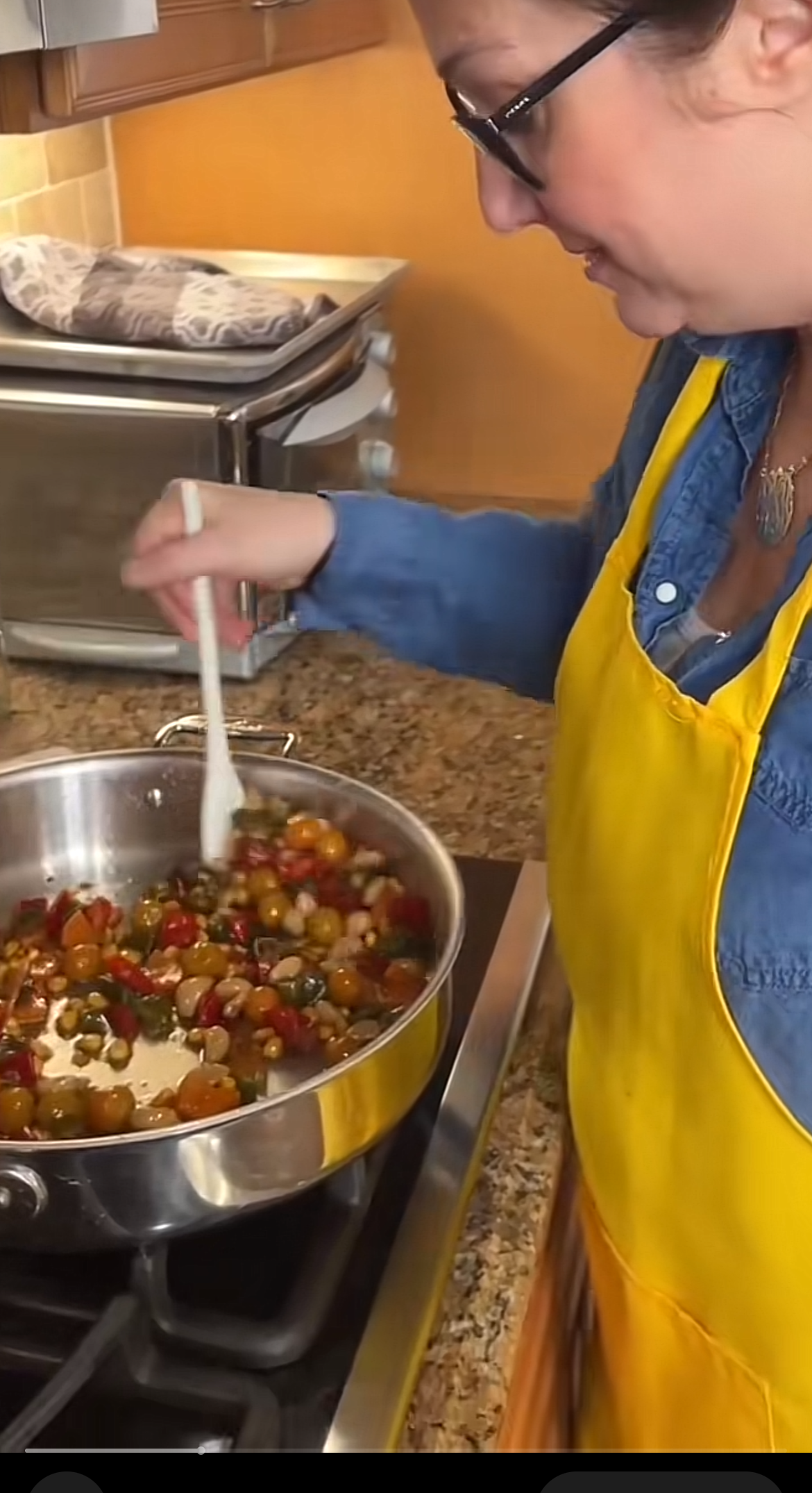 Person in a apron stirring a pan of mixed vegetables on a stove