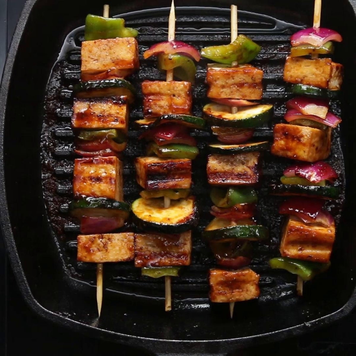 Grilled tofu and vegetable skewers on a grill pan, featuring zucchini, bell peppers, and onions