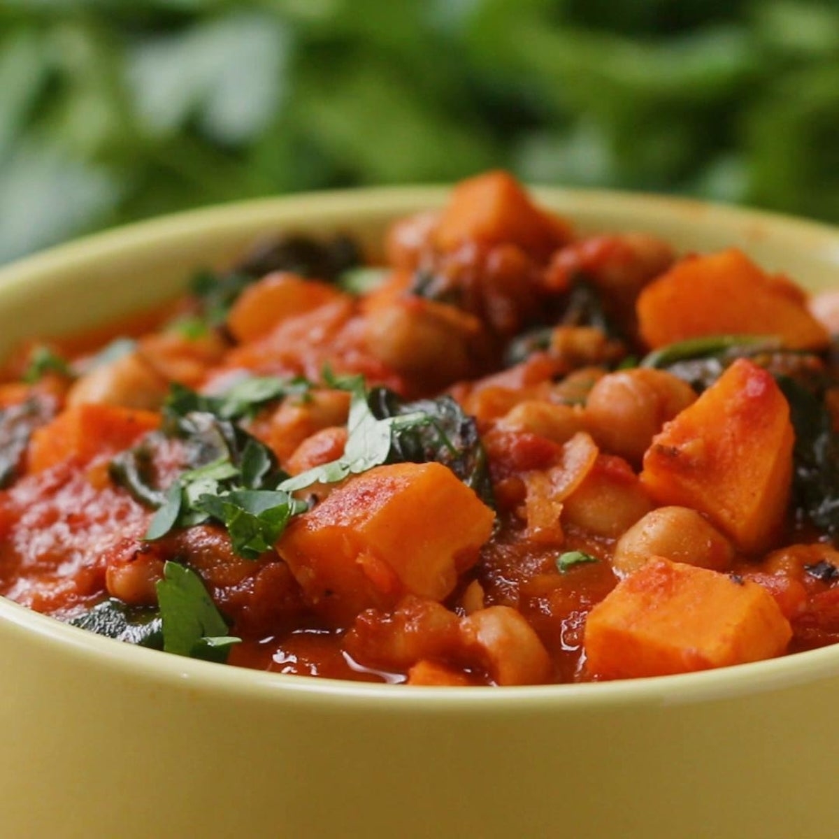 A bowl of hearty stew with chickpeas, sweet potatoes, and leafy greens, garnished with herbs