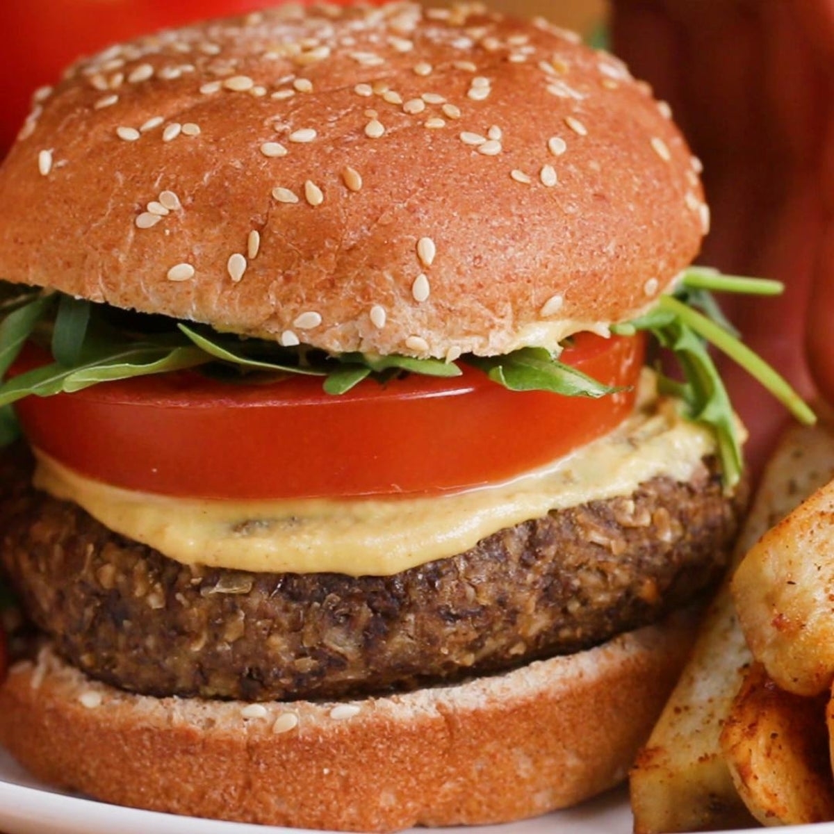 Veggie burger with lettuce, tomato, and hummus in a sesame bun, served with seasoned potato wedges