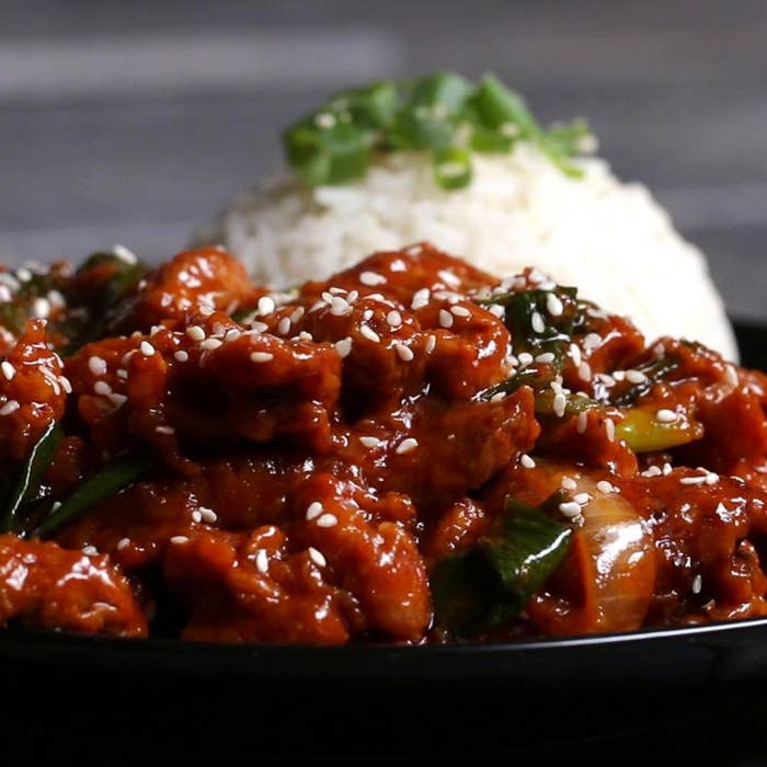 Close-up of a plate featuring sesame pork with green onions, served with a side of white rice garnished with herbs
