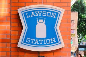 青と白の看板に「LAWSON STATION」とミルク缶のロゴ。下に「OPEN 24 HOURS」と表示。