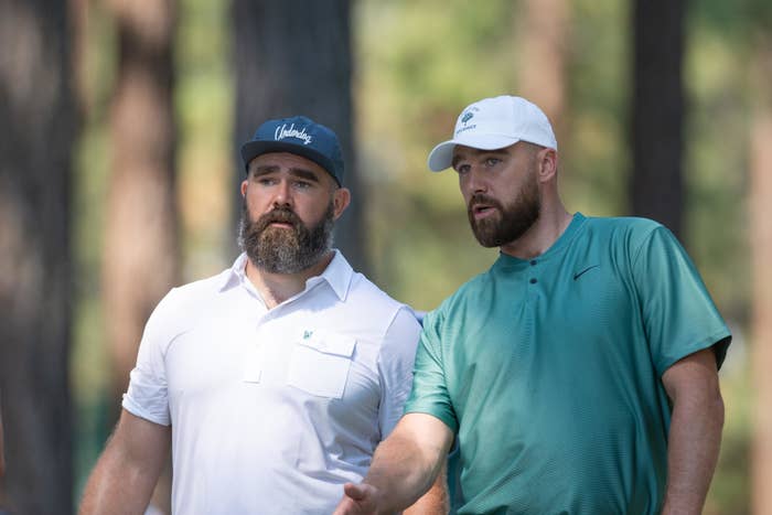 Travis Kelce and Jason Kelce talking on a golf course in collared shirts and hats