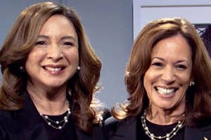 Two women in matching black outfits and necklaces, smiling together on the 'SNL 50' set