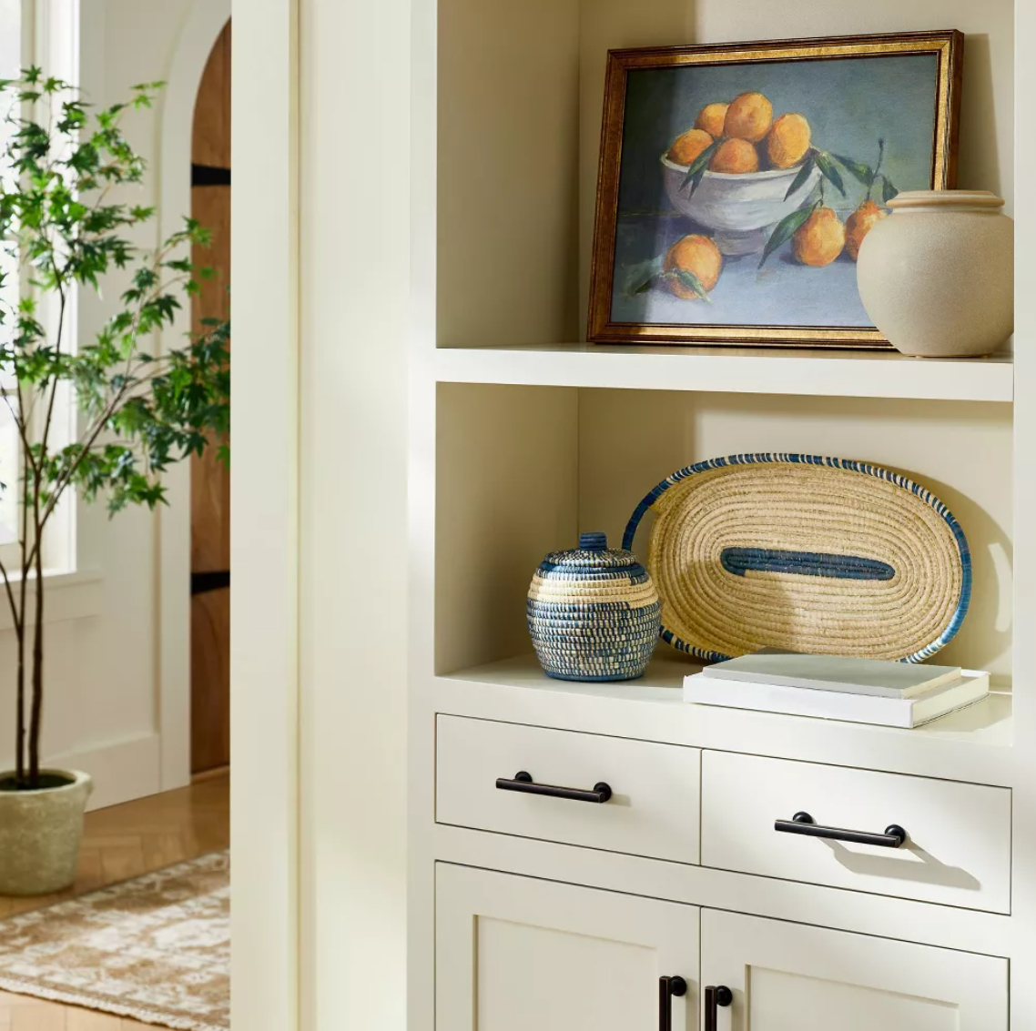 Decorative shelf with fruit painting, woven basket, pottery, and plant in bright room