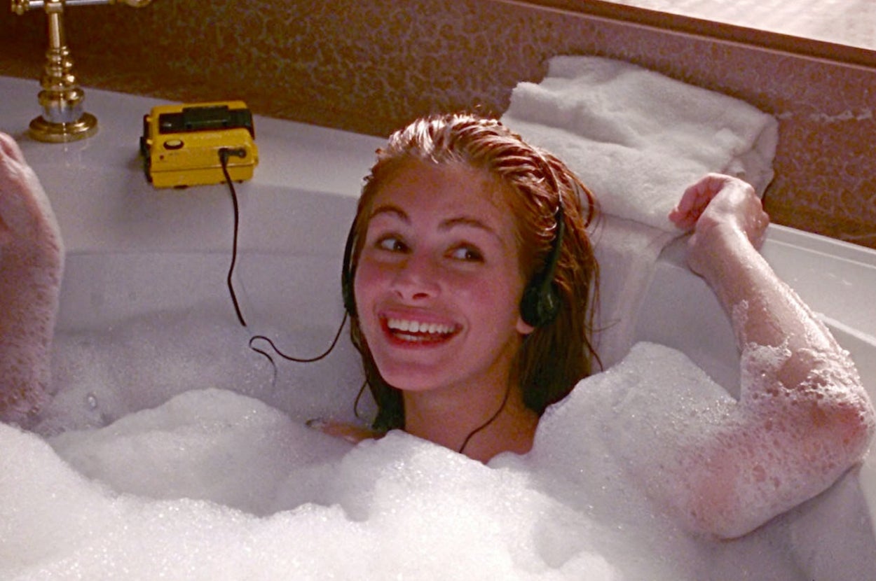 A person smiling in a bubble bath, wearing headphones, with a yellow cassette player nearby