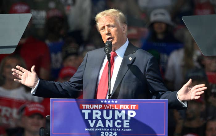 Trump in a suit speaks at a podium displaying the slogan 