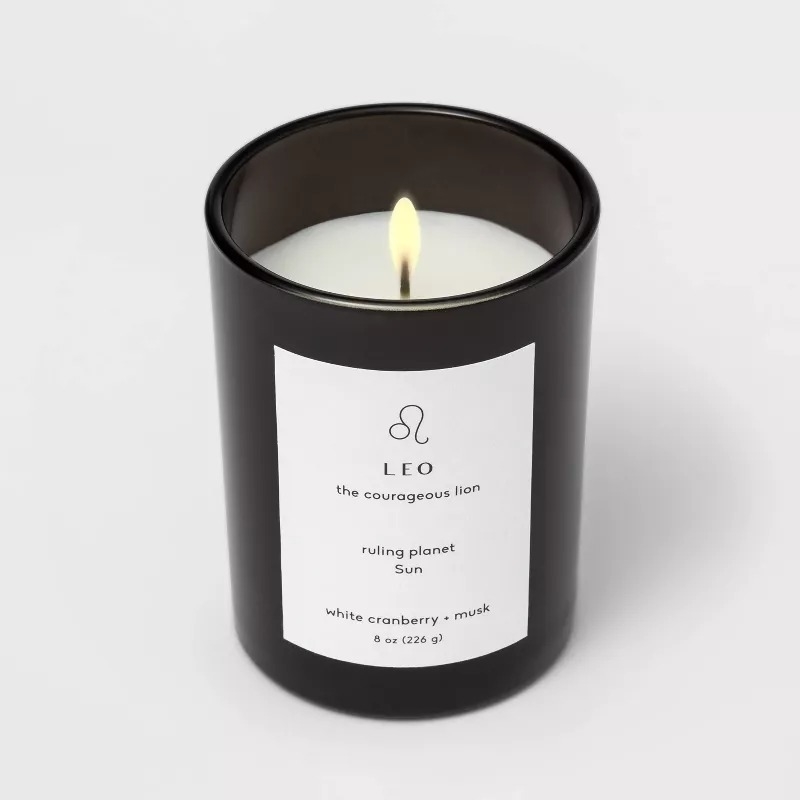 Scented candle in black glass with label reading "Leo: the courageous lion, ruling planet: Sun, white cranberry + musk, 8 oz (226 g)."