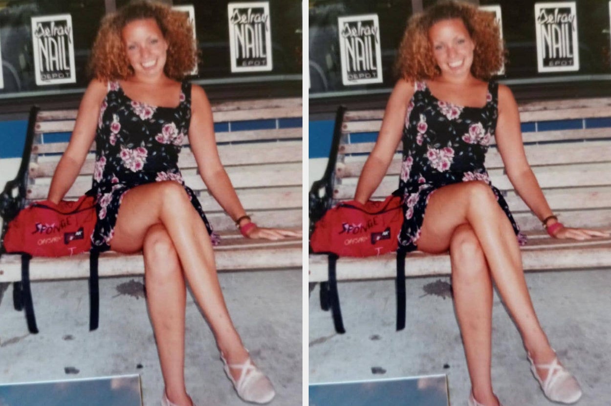 A person with curly hair sits on a bench, smiling. They're wearing a floral dress and light sandals, with a red bag by their side