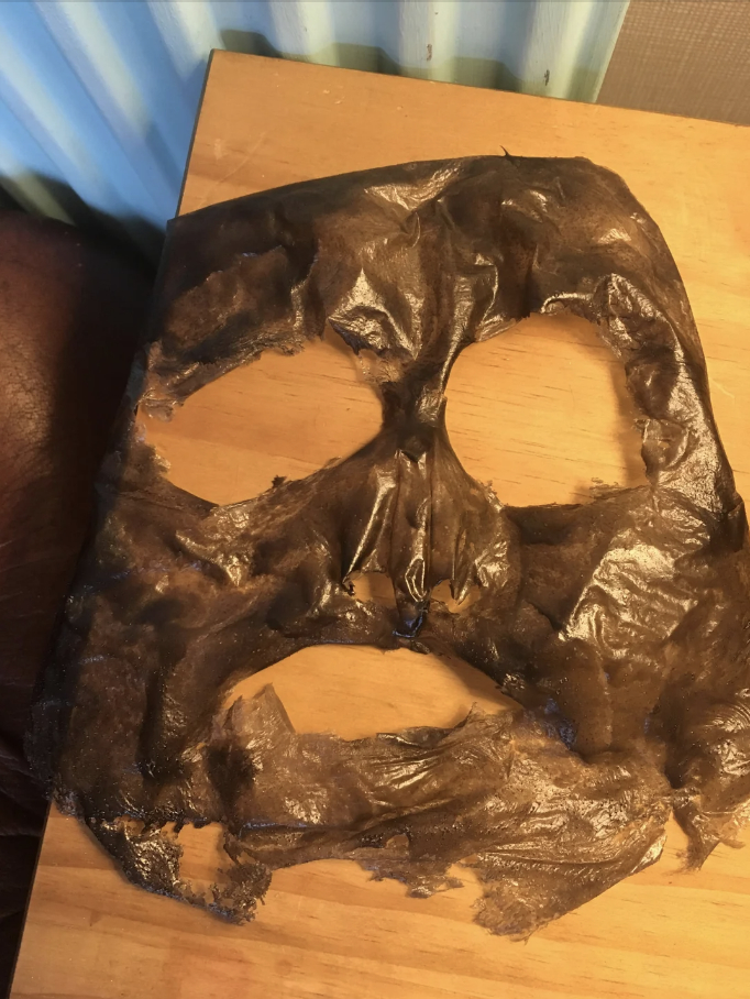 A used, crumpled face mask with eye and mouth holes, lying on a wooden surface