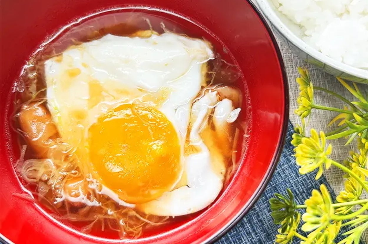 卵がのったみそ汁と白米の食事風景。黄色い花が飾られています。