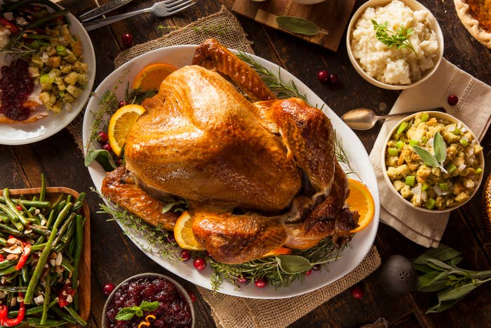 A Thanksgiving dinner table with a roasted turkey, stuffing, mashed potatoes, cranberry sauce, and other dishes. Candles and apples adorn the setting