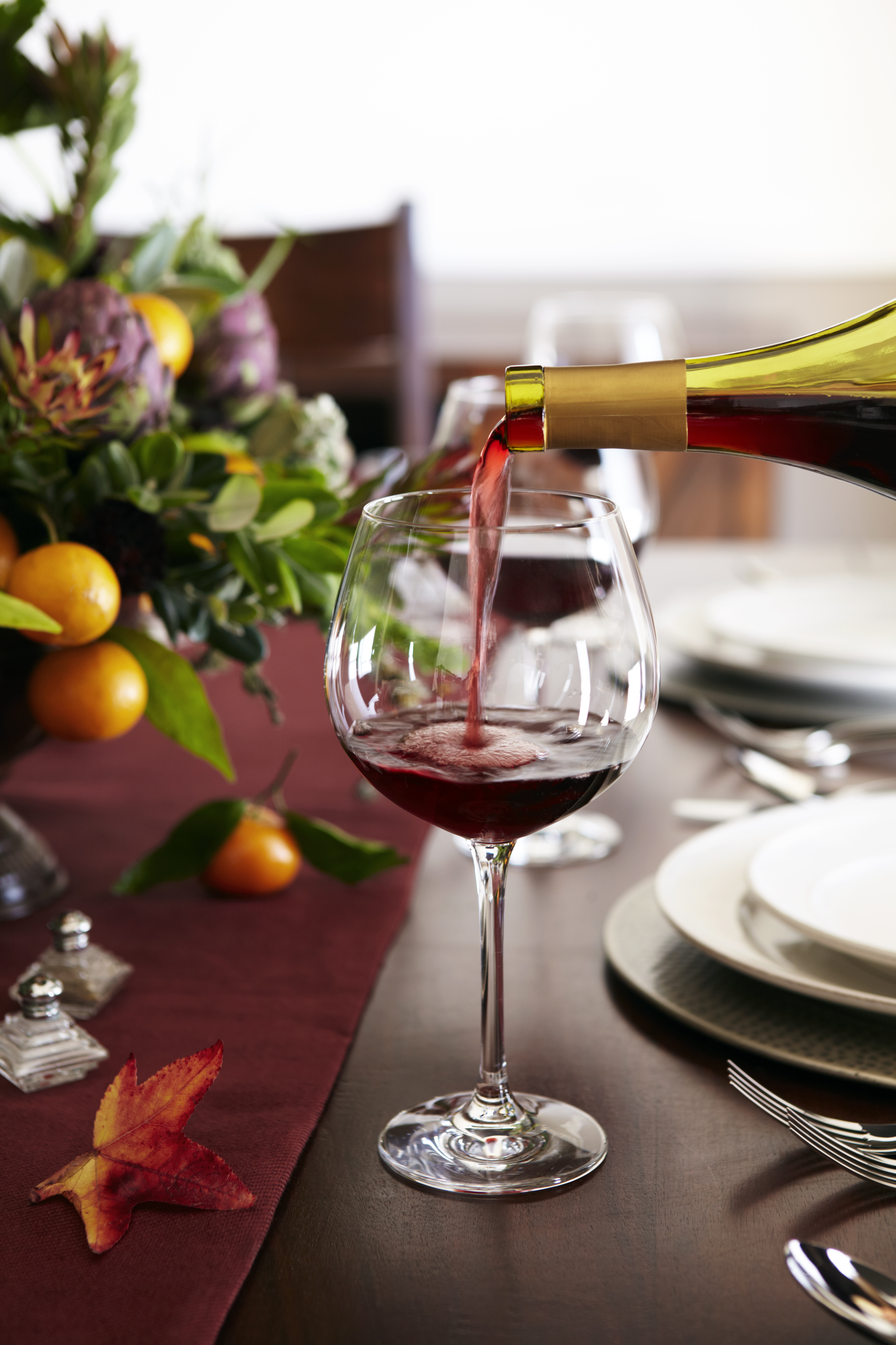 Wine being poured into a glass on a set dining table with a fruit and floral centerpiece