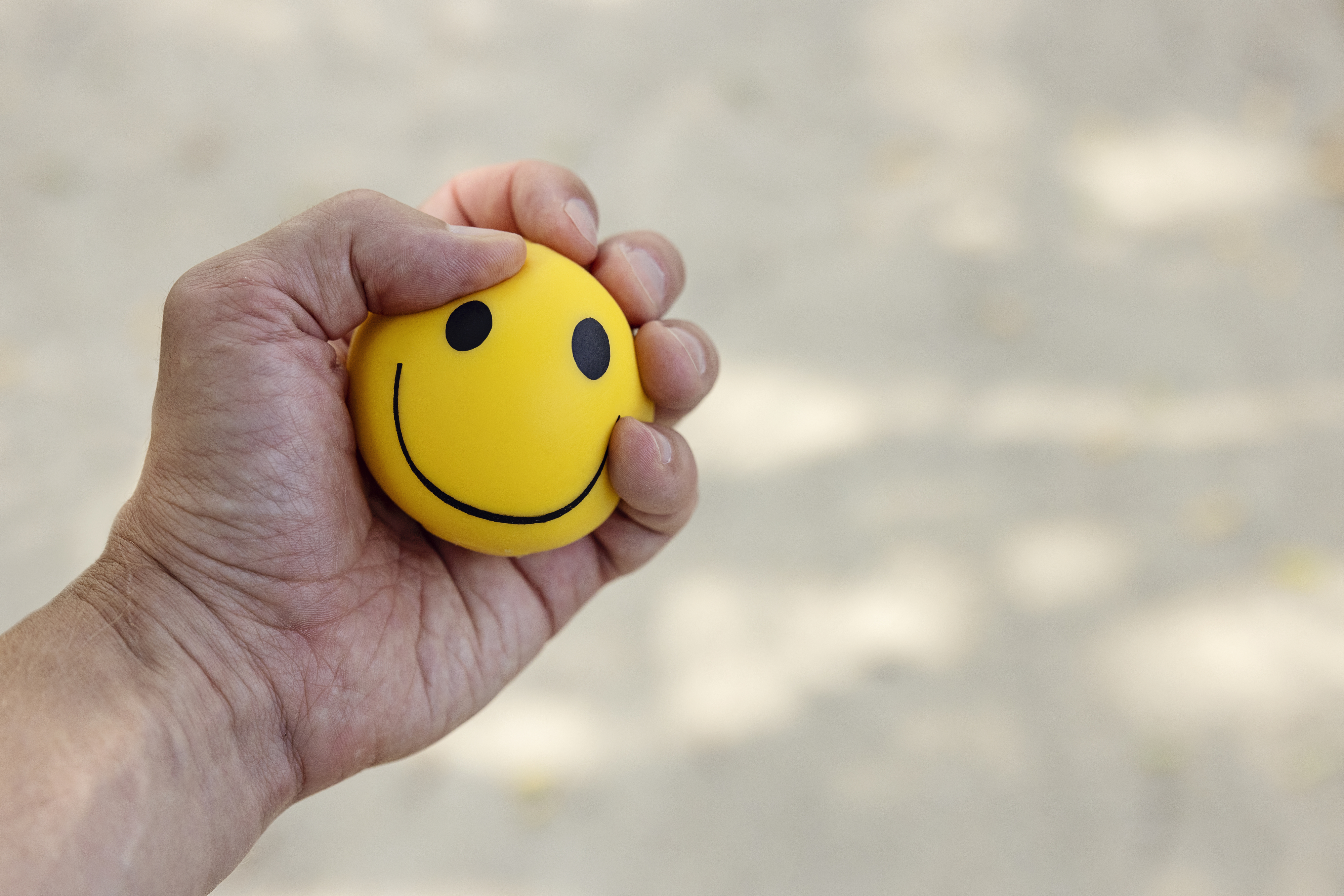 A hand holding a yellow stress ball with a smiley face on a light background