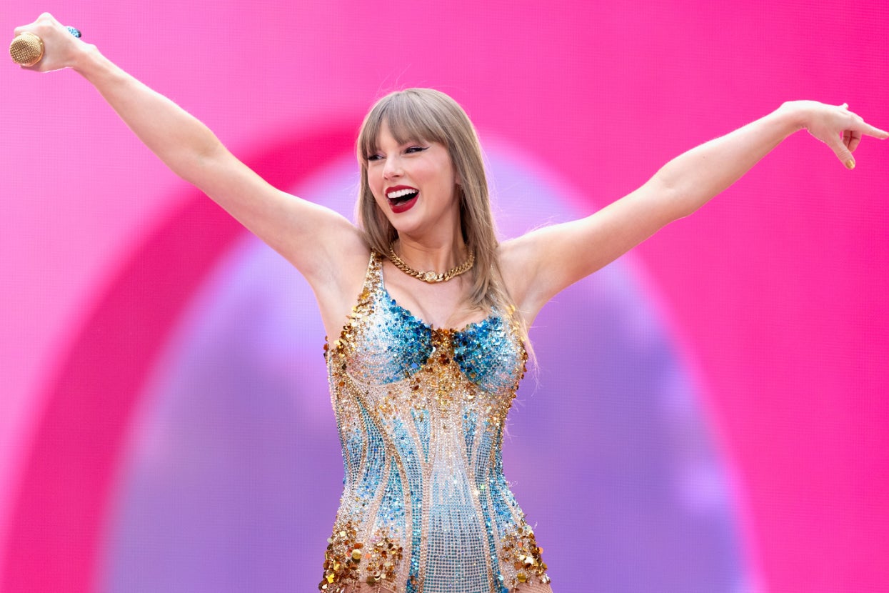 Taylor Swift on stage with arms raised, wearing a sparkly, fitted bodysuit