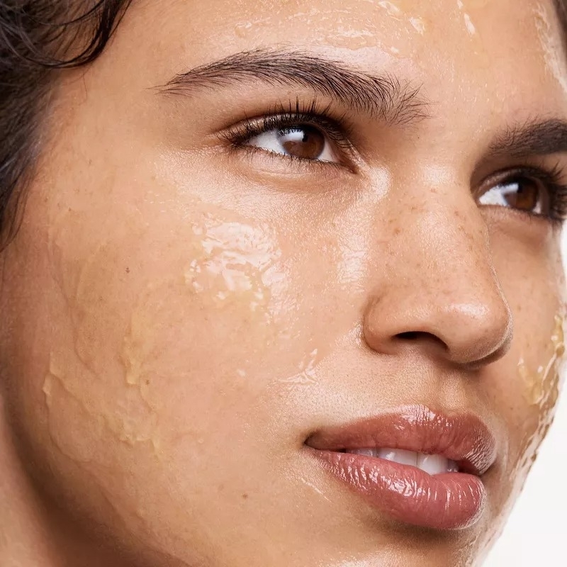 A person with glossy skincare product on their face, looking to the side