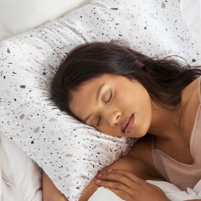 A person is peacefully sleeping on a speckled pillow, lying on their side