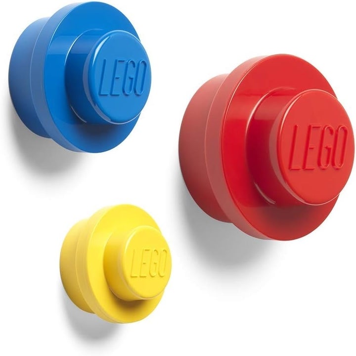 Three large, circular wall hooks shaped like LEGO bricks in blue, yellow, and red