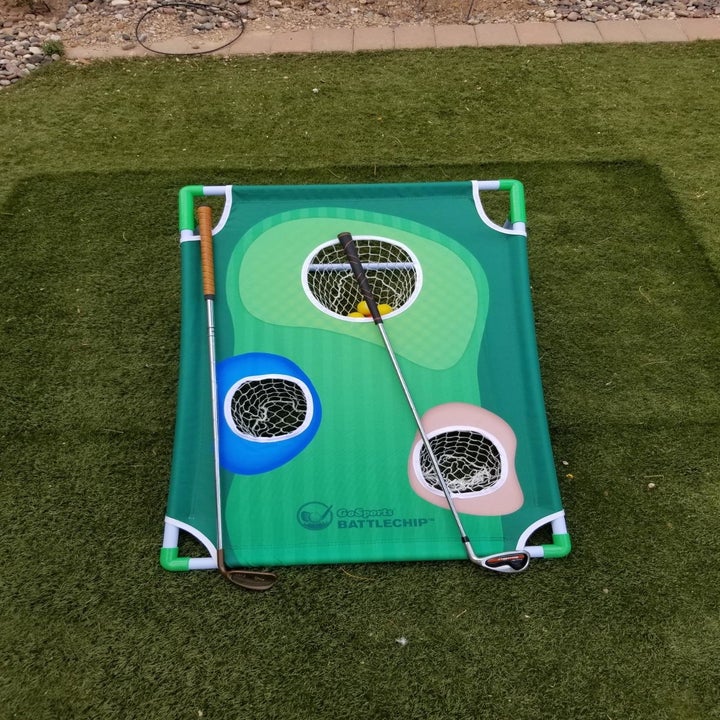 Golf chipping game mat outdoors with three target holes and a golf club