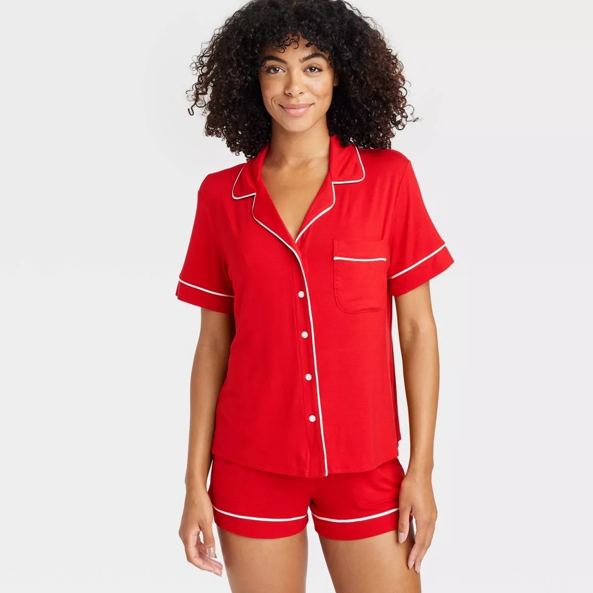 Person wearing a red pajama set with white trim, consisting of a short-sleeve button-up top and shorts