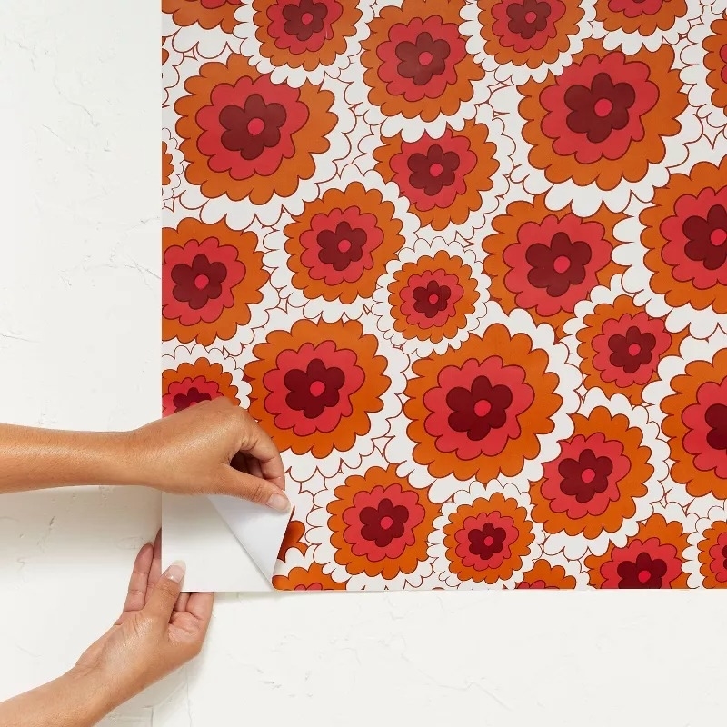 Hands applying floral-patterned wallpaper with layered flower designs in various shades