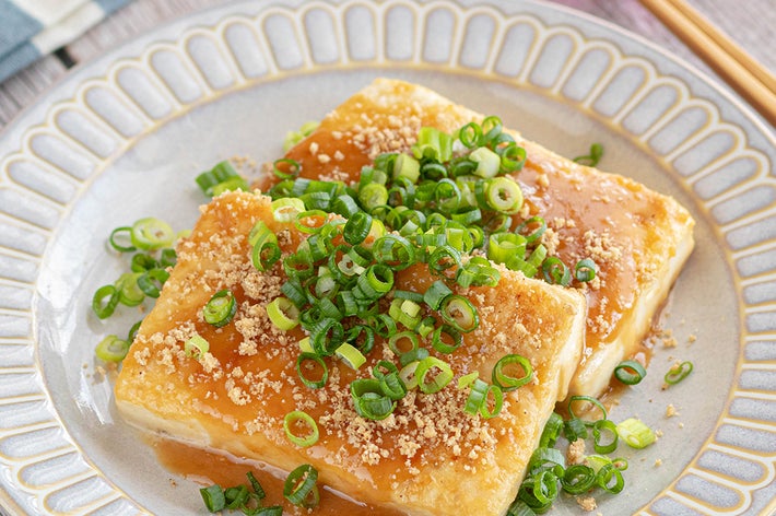 ネギをのせた2切れの豆腐にソースがかかった料理。プレートに盛られた美味しそうな一品。