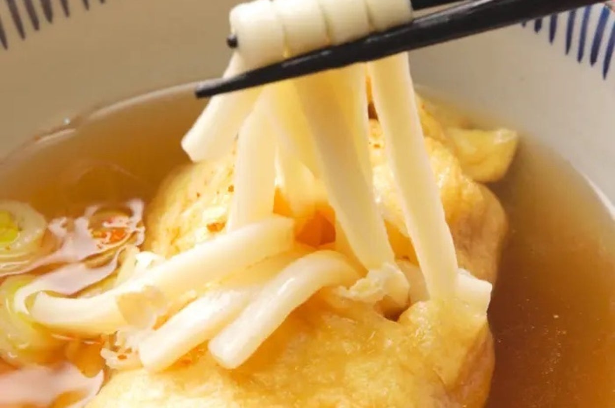 器に入ったうどんを箸でつまんでいる様子。薄いスープに油揚げが浸かっています。