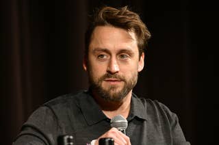 Kieran Culkin holding a microphone, wearing a casual shirt, speaking in a dimly lit setting