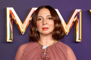 Person with bob haircut and elegant, semi-sheer dress stands in front of large decorative letters
