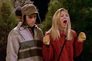Two people outdoors; one wears a deerstalker hat and coat, looking surprised. The other is wearing a coat, yelling with hands in gloves raised