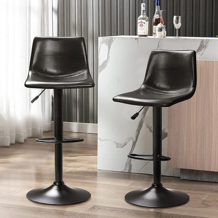 Two modern black bar stools with footrests and adjustable height, placed near a marble counter