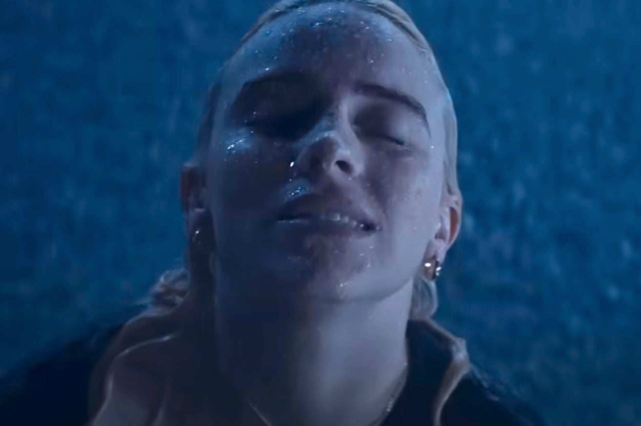 Billie Eilish with wet hair looks upward, water droplets on face, wearing earrings