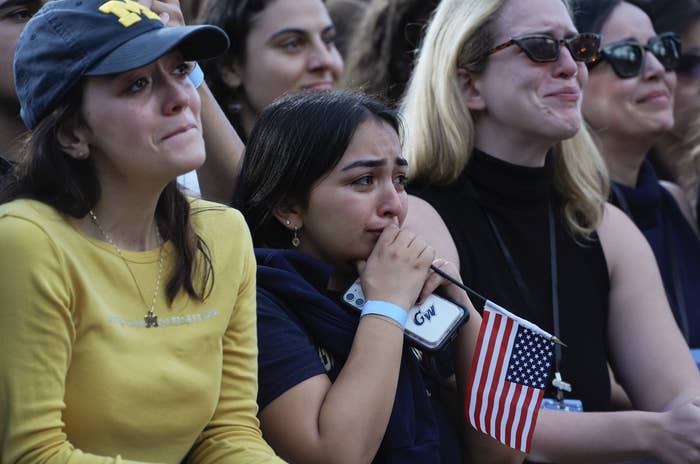 A group of people with emotional expressions; one holds a small American flag and a phone with the name "Gigi" visible