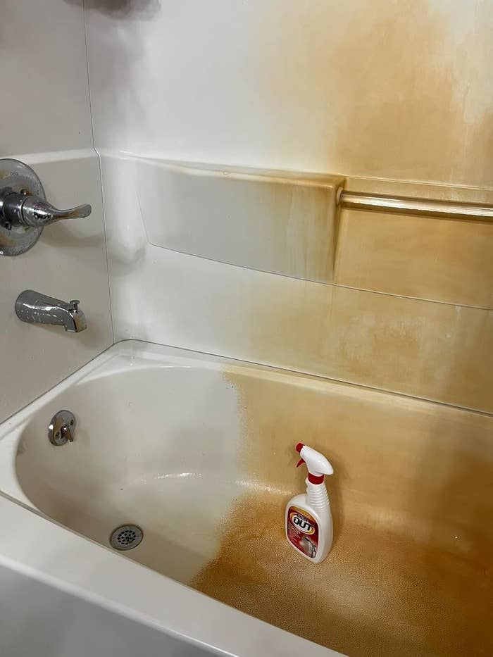 Bathtub with prominent rust stains, featuring a spray bottle of cleaning product placed on the tub surface