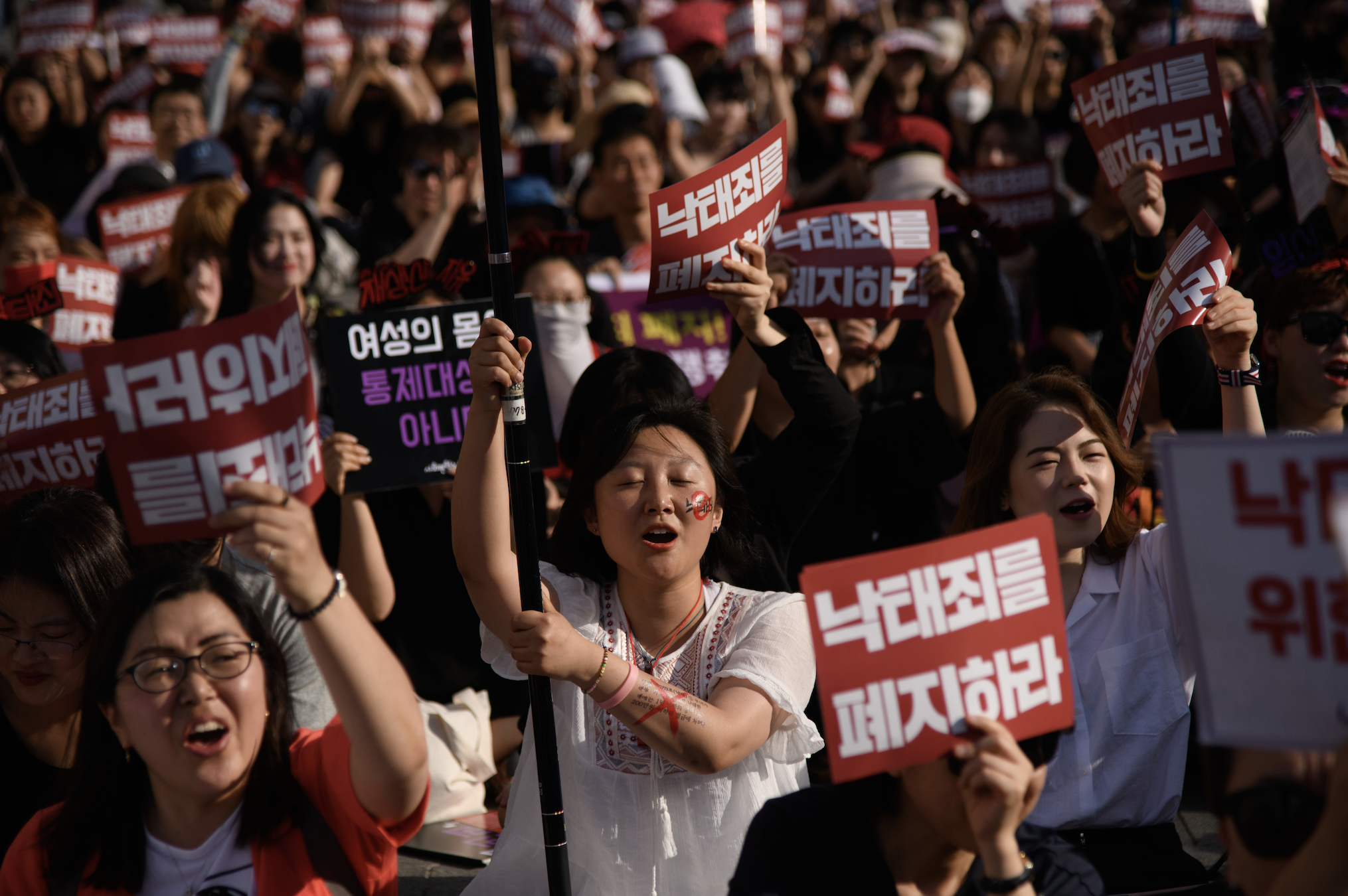 A large group of protesters hold signs with Korean text, gathered in a demonstration, showing strong expressions of solidarity and activism