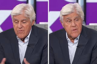 An older man in a suit speaks during an interview, gesturing with his hands
