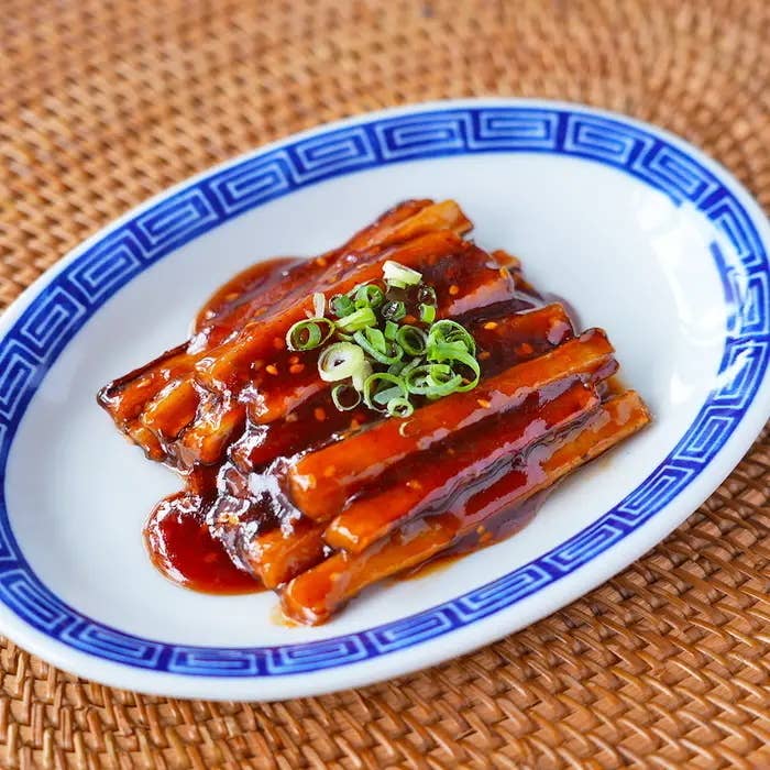 白い皿に盛られたタレで覆われたヤンニョムごぼう。細かく刻まれたネギが上に飾られている。