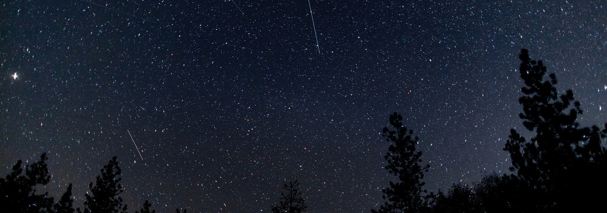 星空が広がる夜空の下、湖が静かに広がっている風景。流れ星が見える。