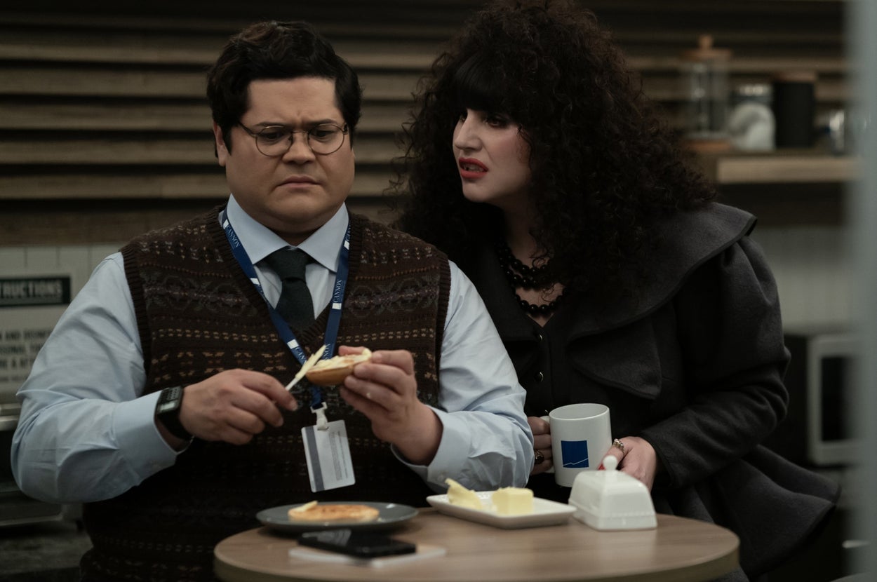 Guillermo spreads butter on toast while Nadja holds a mug, leaning in and speaking intently