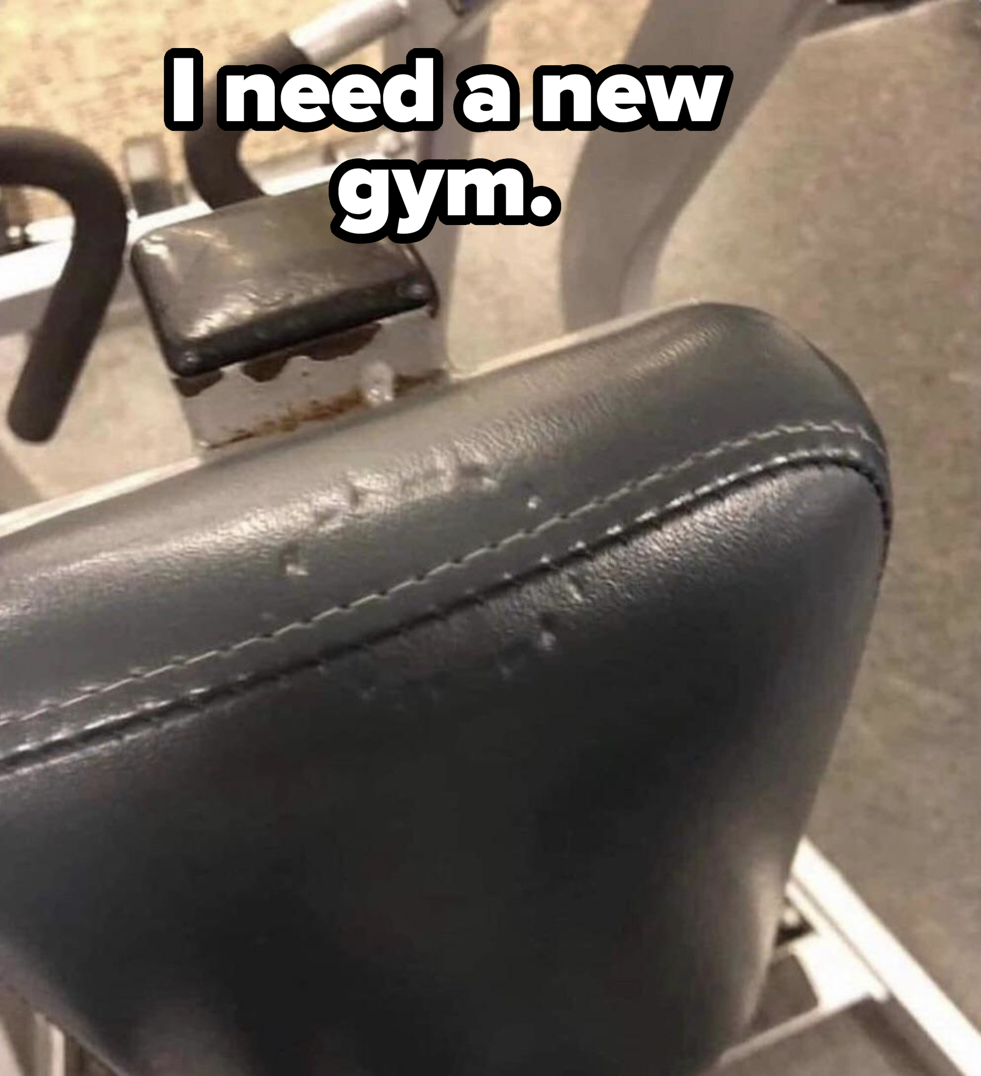 Worn-out seat of a gym exercise machine, showing visible signs of wear and tear