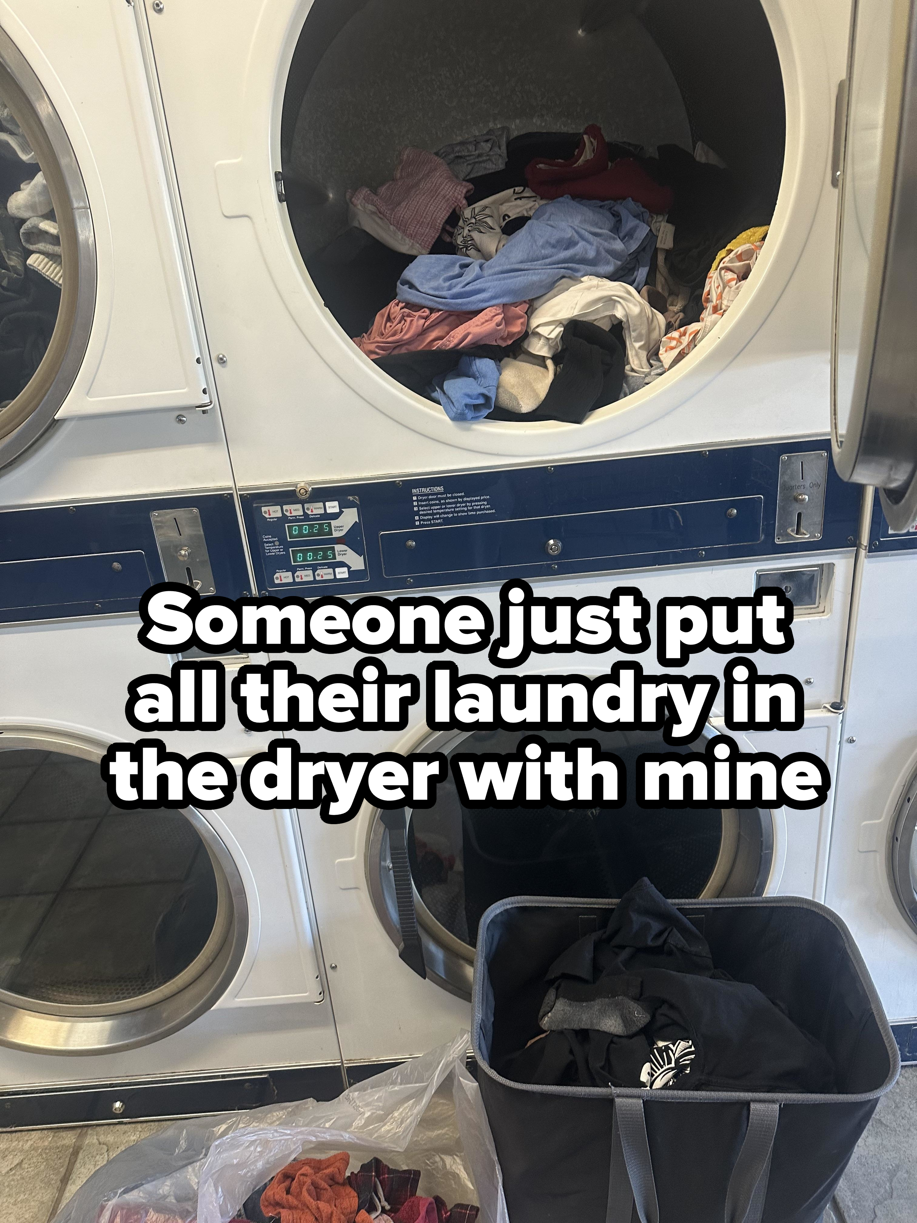 Clothes in a laundromat dryer with a basket nearby filled with more clothing