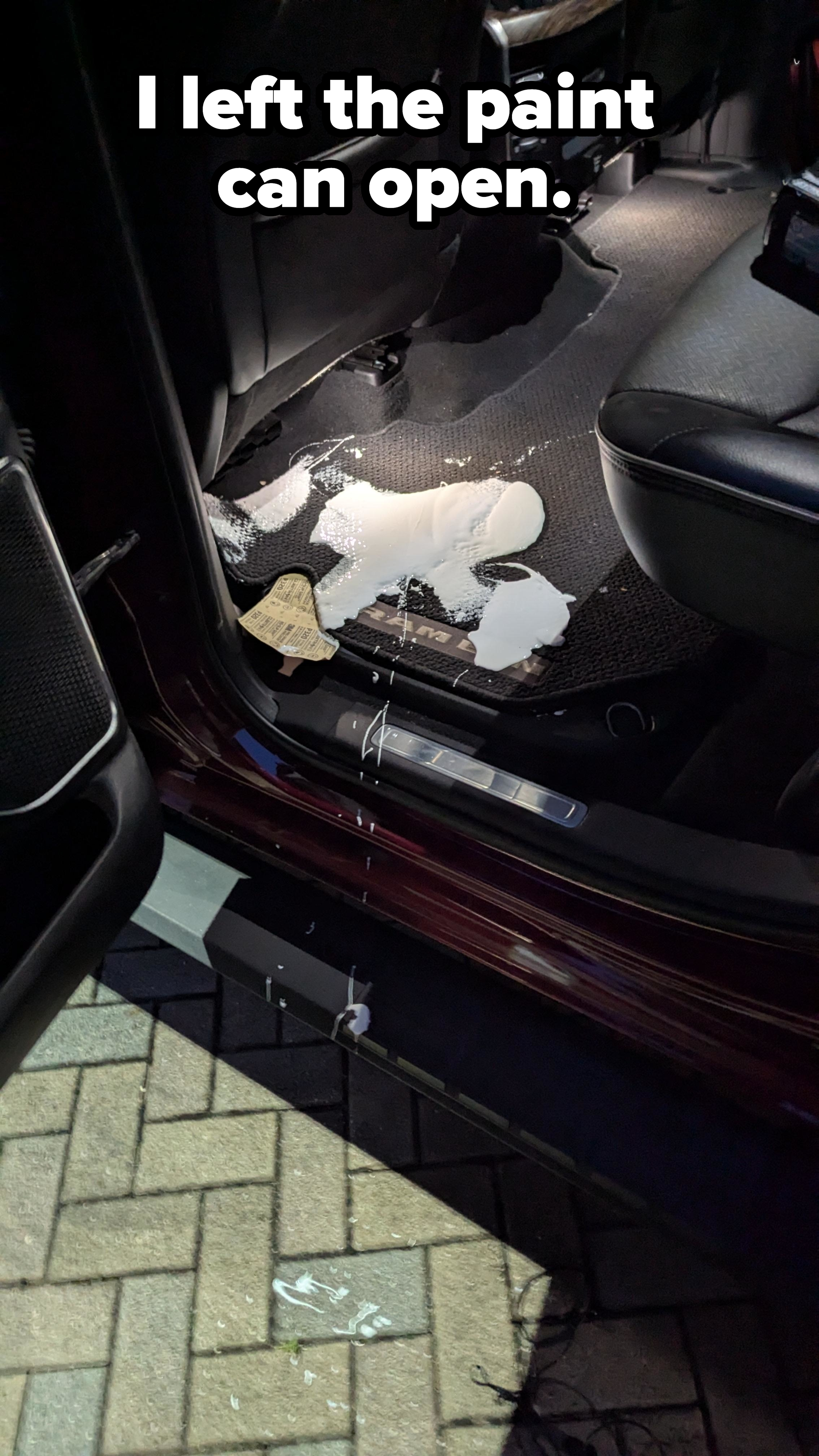 Spilled white liquid on a car floor near the open door, with visible floor mats and a brick pavement outside