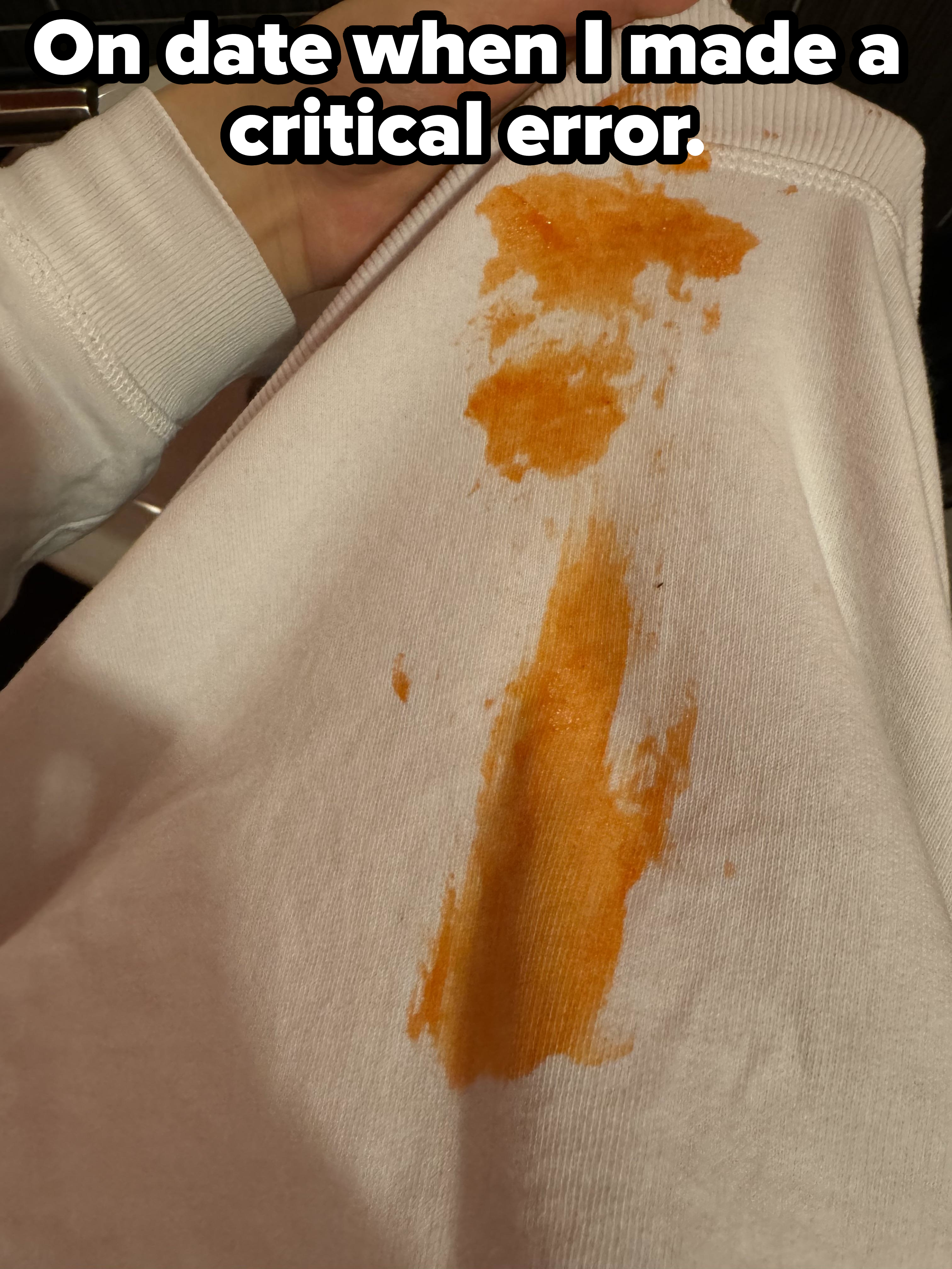 Hand holding a white shirt stained with an orange substance