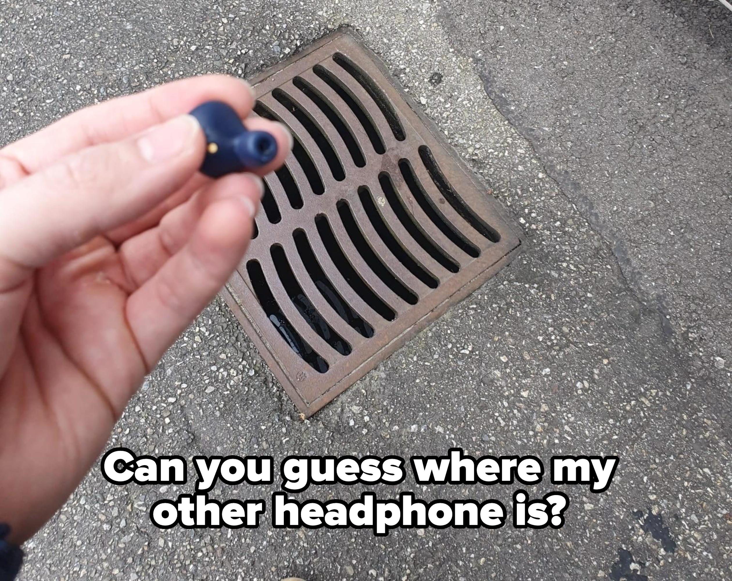 A hand holds a wireless earbud above a street drain, suggesting a potential fall or mishap