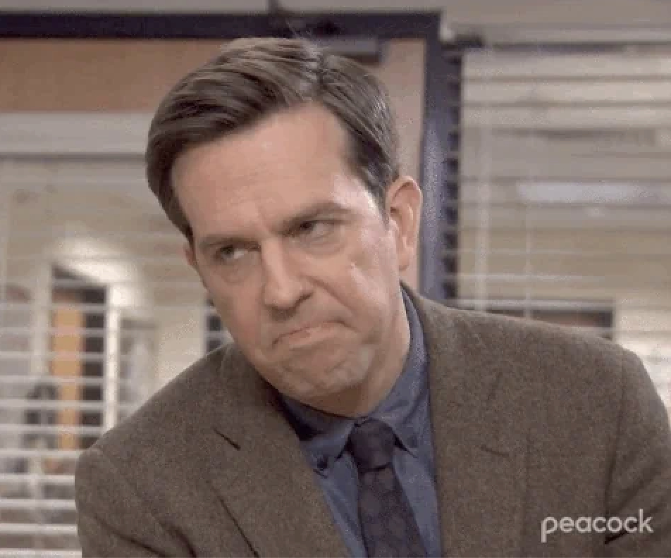 Andy from The Office rolling eyes in an office setting, wearing a suit jacket and tie, with blinds in the background