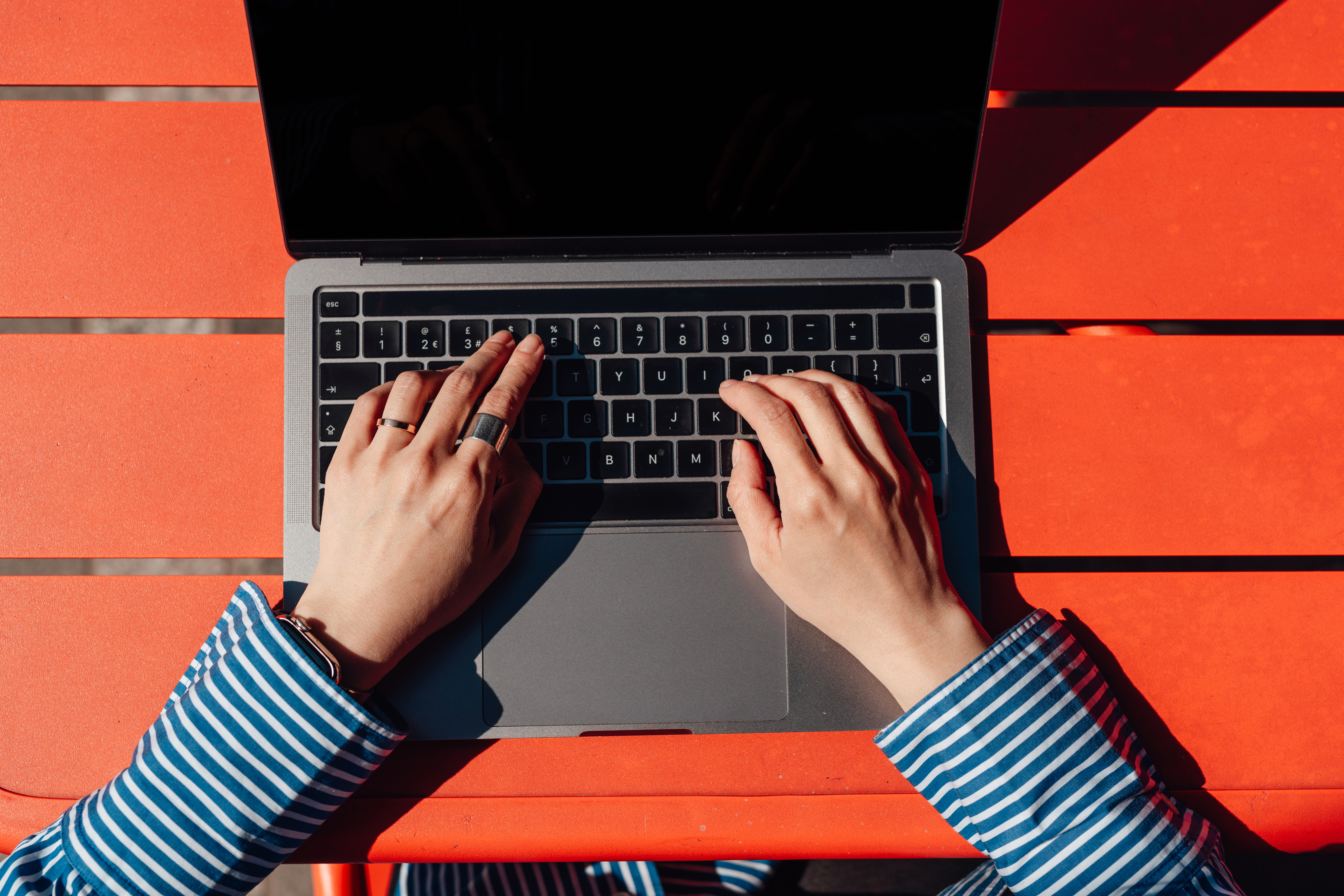 Hands typing on a laptop on a table. The person is wearing a striped long-sleeve shirt